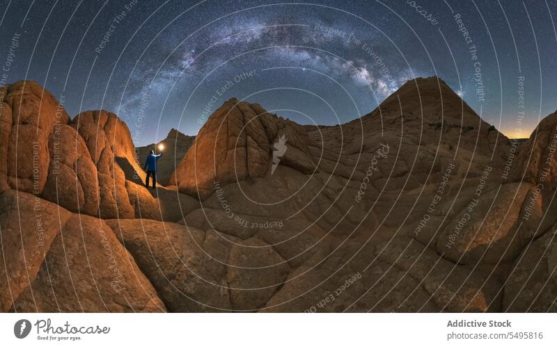 Anonymous person with flashlight on rocky formation in valley under starry sky tourist traveler admire desert silhouette night explore mount Vermilion Cliffs