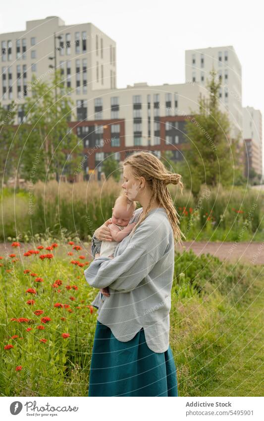 Woman carrying and kissing baby in park against sky mother head woman love small hug adorable family lifestyle cute dreadlocks infant together cuddle motherhood