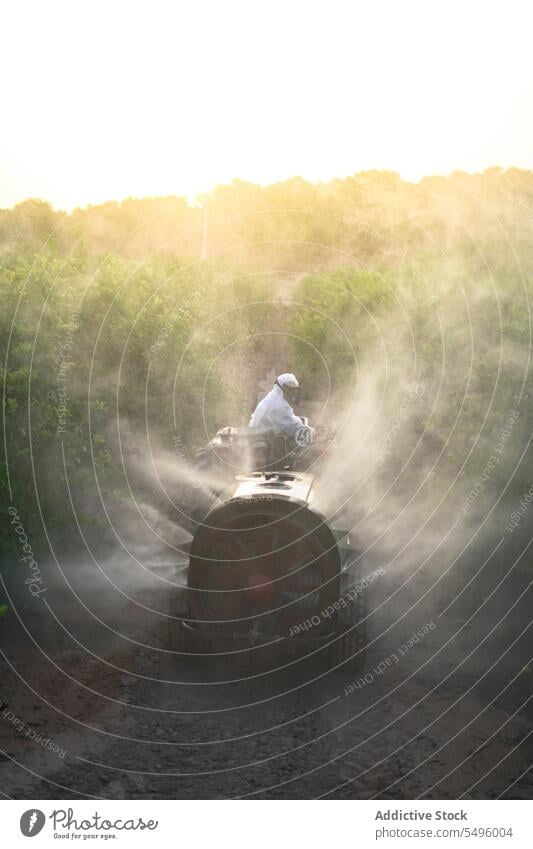 Anonymous farmer spraying pesticide on lemon trees while riding tractor insecticide agriculture protective suit mask chemical nature countryside cultivation