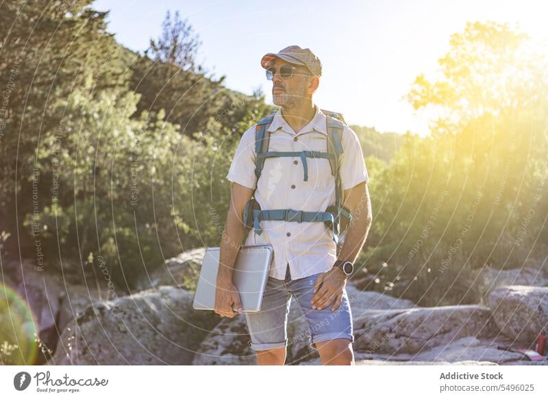 Man with laptop and backpack on cliff man hiker nature forest traveler rock summer journey male adventure rocky green gadget device environment woods activity