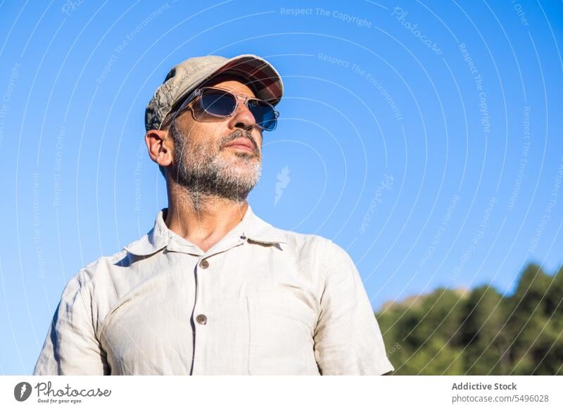 Confident bearded man in sunglasses and cap confident summer blue sky serious brutal appearance male unshaven individuality nature eyewear personality accessory