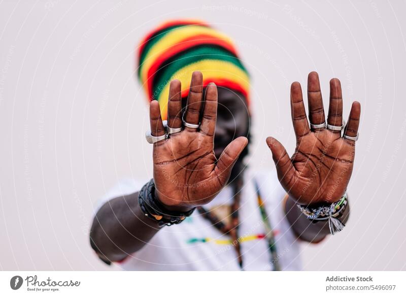 Blurred African American man in colorful hat standing and looking at camera while putting hands in front of the camera african american ethnic crop clothing