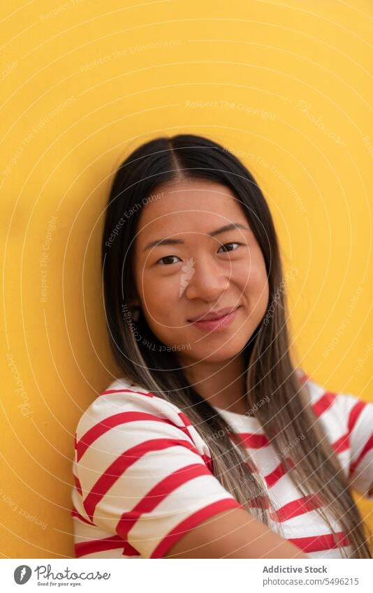 Smiling woman in eyeglasses sitting against yellow wall positive happy casual smile stripe portrait glad optimist fashion pleasure pleasant asian confident