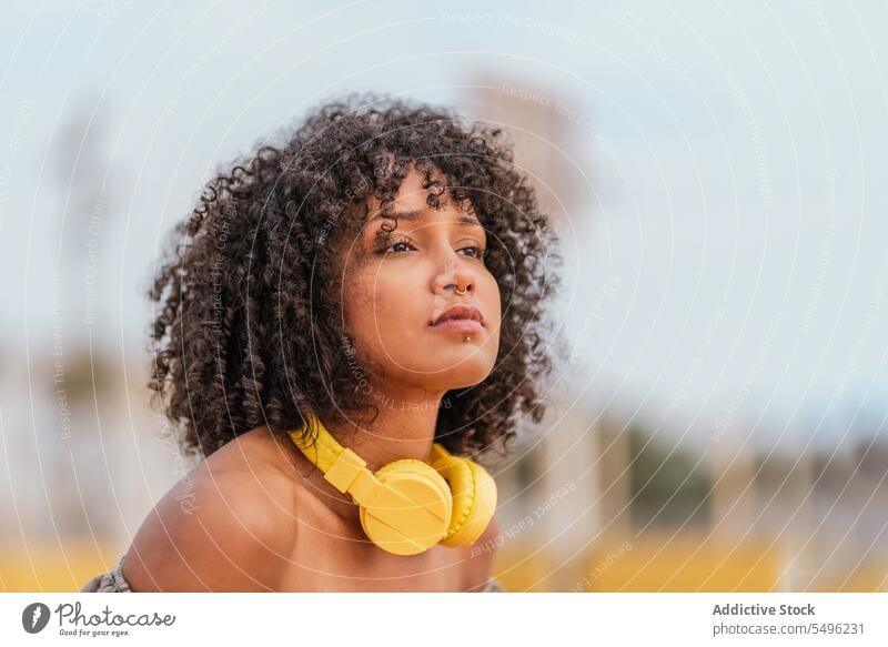 Young woman with headphones curly hairstyle looking away headshot pensive portrait headset audio trendy alone human face concentrate fashion lifestyle