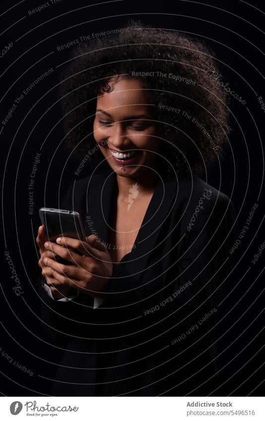 Smiling ethnic woman with smartphone in black studio using browsing smile happy positive online message mobile hispanic female young gadget device cheerful