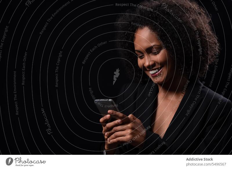 Smiling ethnic woman with smartphone in black studio using browsing smile happy positive online message mobile hispanic female young gadget device cheerful