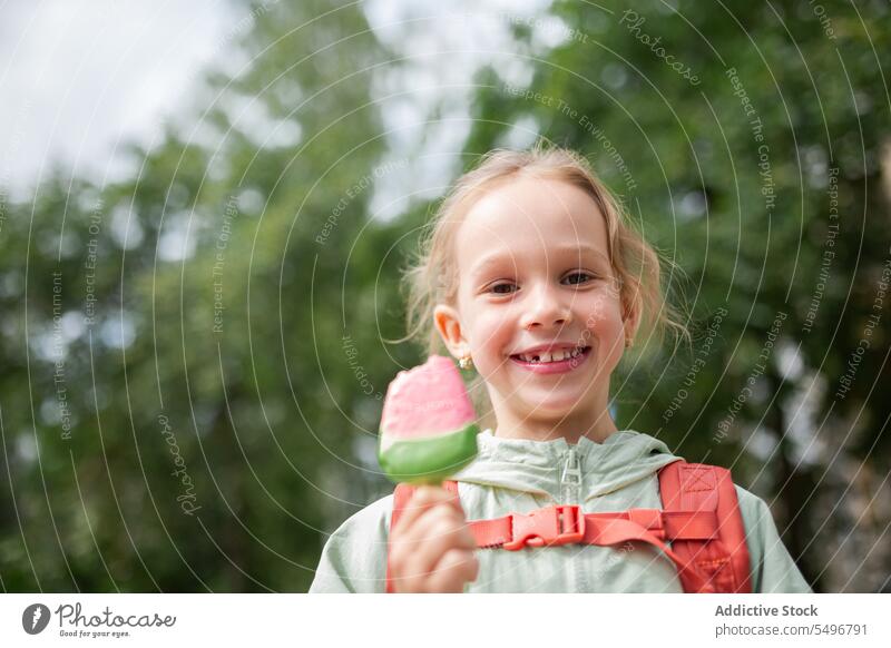 Girl with backpack standing near grassy field and enjoying ice cream child park path cute childhood green kid girl adorable summer sweet carefree wavy hair