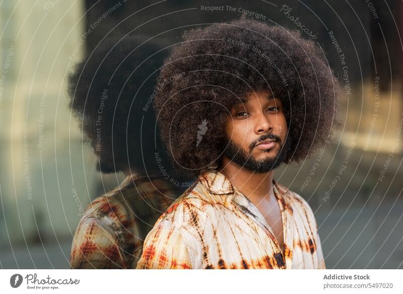 Guy with Afro hairstyle looking at camera against mirrored wall man street appearance curly hair reflection afro portrait male beard shirt ethnic guy hispanic