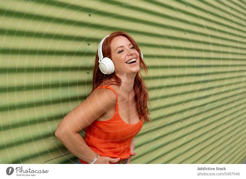 Happy woman listening to music against green wall headphones happy smile cheerful using dance leisure carefree casual female young joy lifestyle modern device