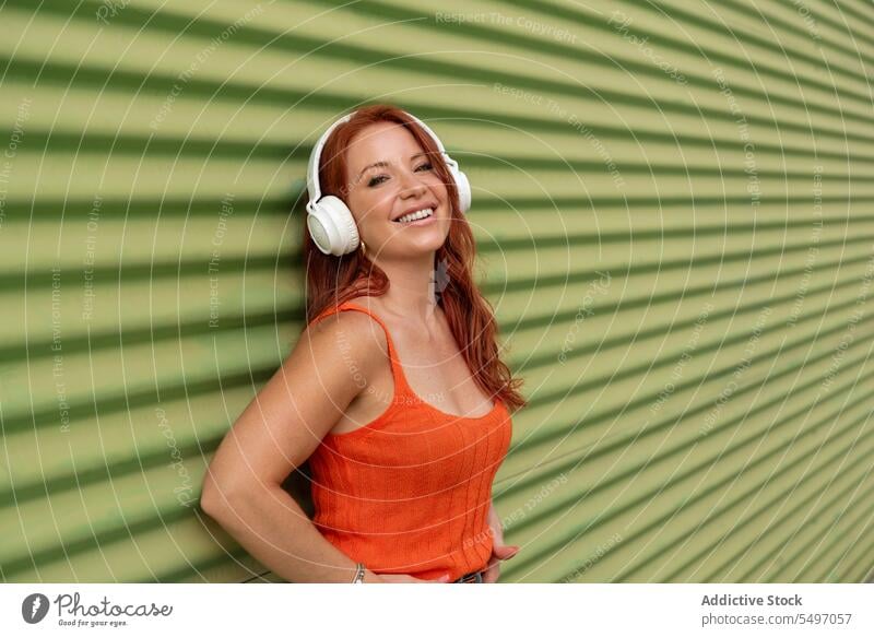 Happy woman listening to music against green wall headphones happy smile cheerful using leisure carefree casual female young joy lifestyle modern device song