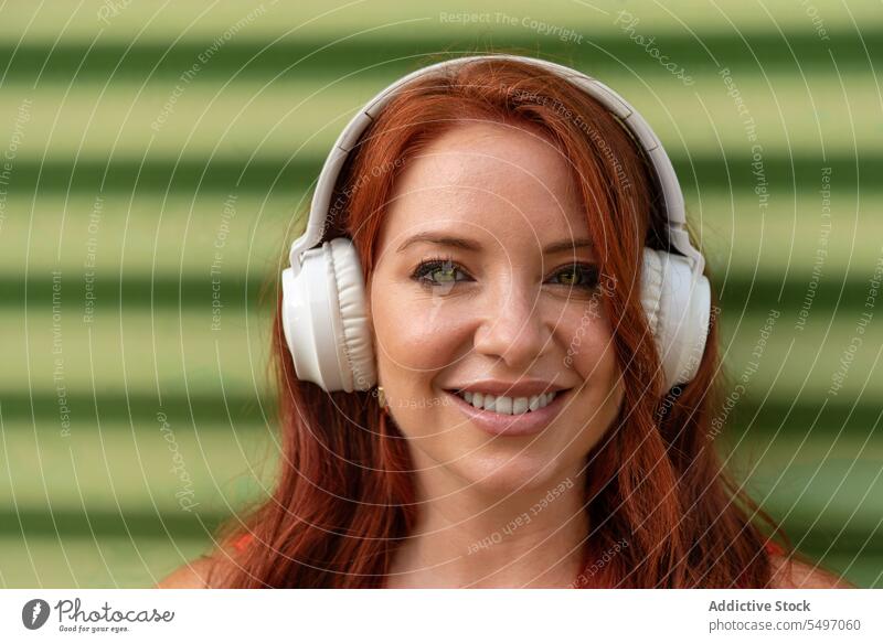 Happy woman listening to music against green wall headphones happy smile cheerful using dance leisure carefree casual female young joy lifestyle modern device