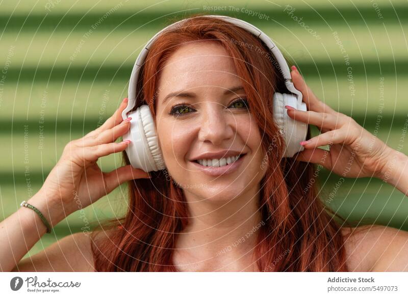 Happy woman listening to music against green wall headphones happy smile cheerful using leisure carefree casual female young joy lifestyle modern device song