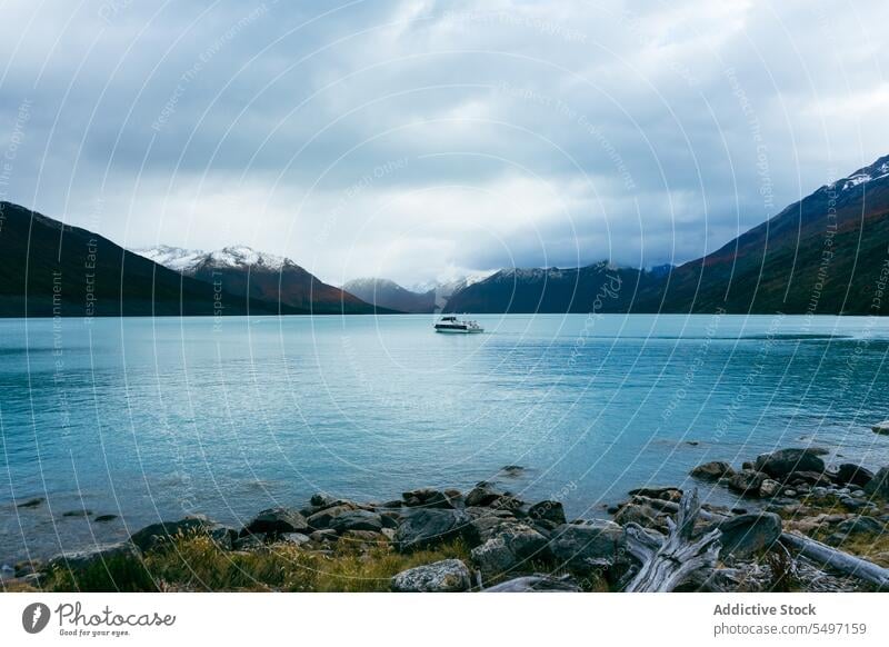 Boat floating on calm lake by icy mountain ridge glacier boat landscape shore iceberg rocky nature cloudy snow water cold log coast winter sky scenic lakeside