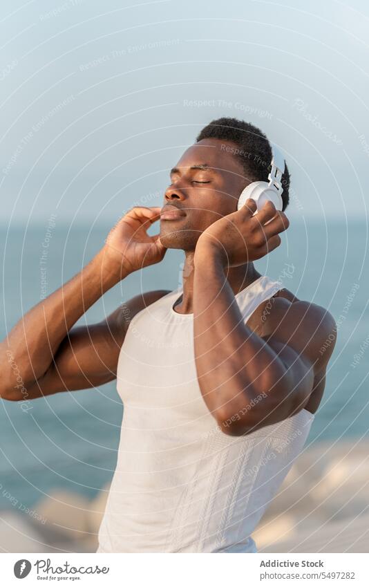 Thoughtful black man with headphones near sea music listen pensive song wireless sound device male water melody calm tranquil dreamy african american