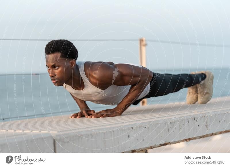 Strong black man doing plank exercise on parapet training workout determine athlete sport activity sea male endurance african american sportsman strong