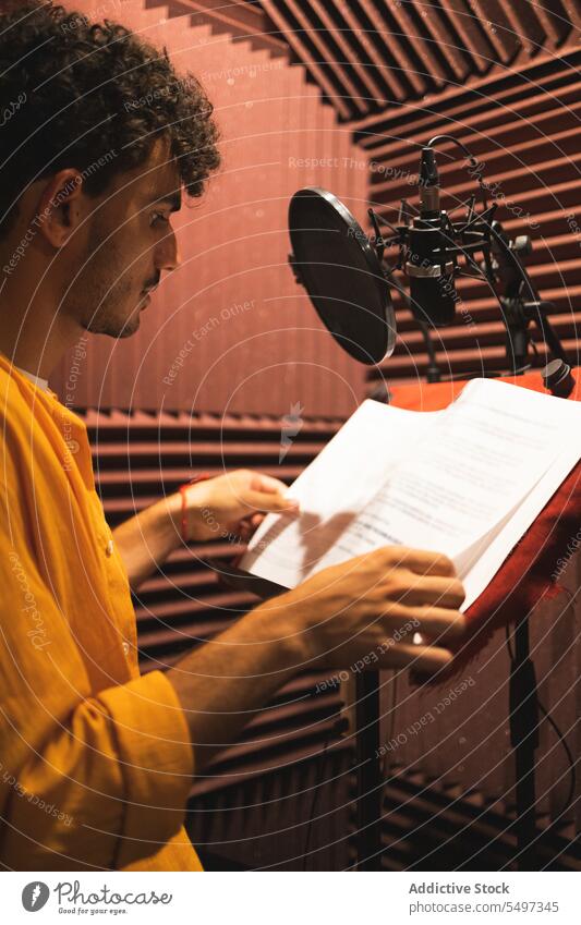 Thoughtful young ethnic man sitting and reading papers on desk in studio microphone serious hand at chin thoughtful pensive touch chin male hispanic curly hair