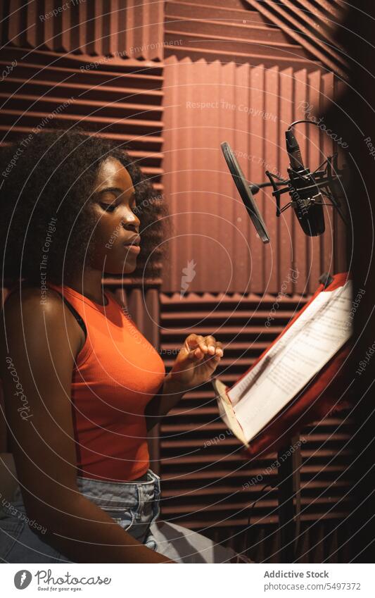 Focused black female standing and recording song near microphone equipment in studio woman singer paper focus audio young african american ethnic read sound