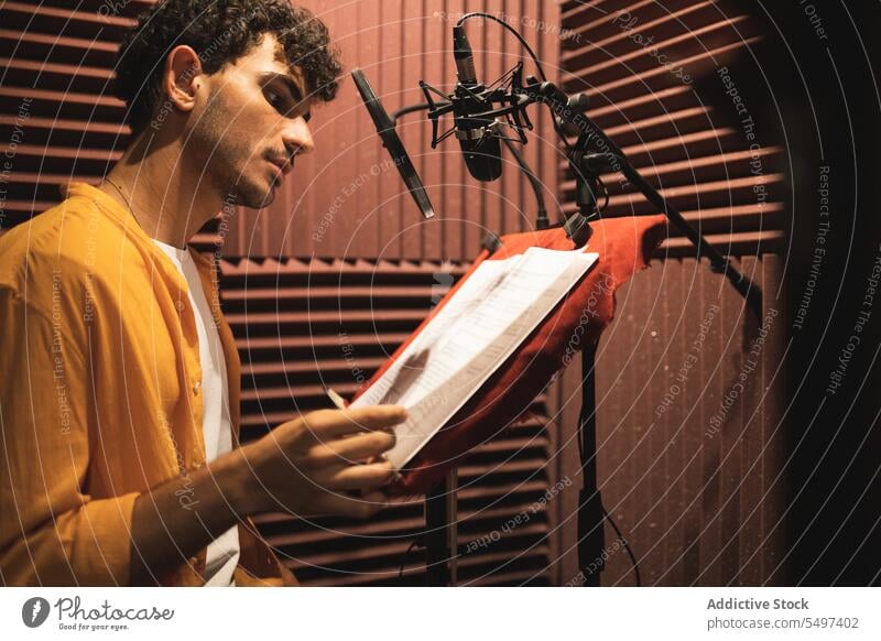 Thoughtful young ethnic man sitting and reading papers on desk in studio microphone serious hand at chin thoughtful pensive touch chin male hispanic curly hair