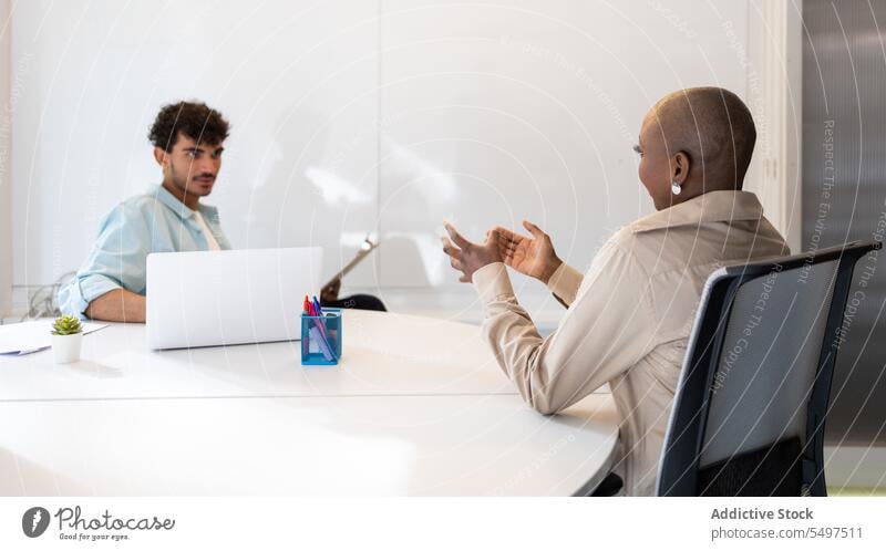 Diverse colleagues discussing project in office while sitting at table with laptop man woman speak professional conversation female young african american