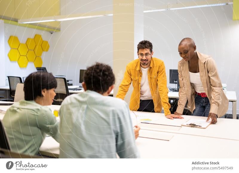 Diverse colleagues standing and discussing with unrecognizable colleagues at table man woman talk project conversation smile together communicate male female