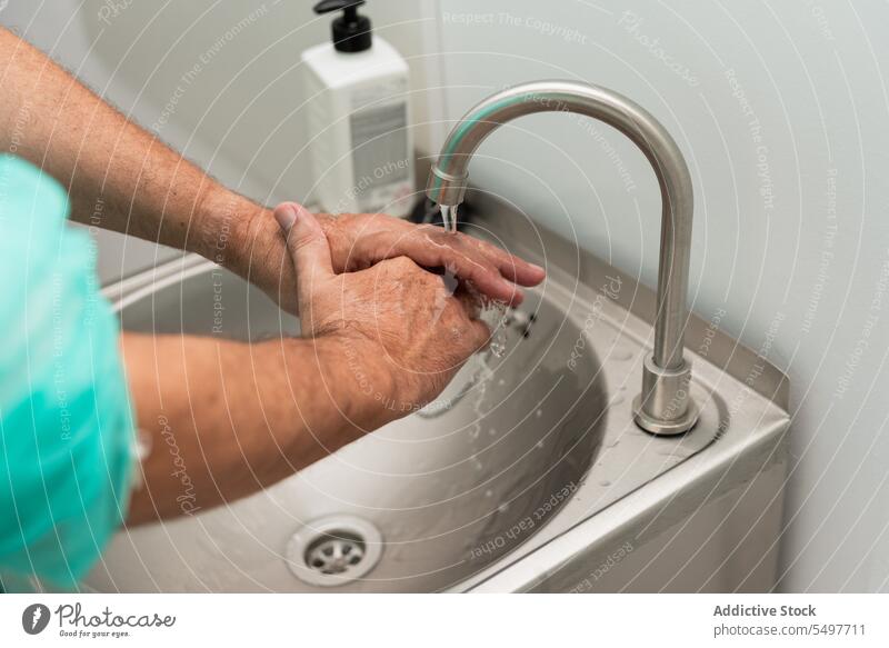 Crop anonymous surgeon washing hands before operation man doctor surgery operating room prepare sterile clean hygiene sanitary male uniform sink tap water