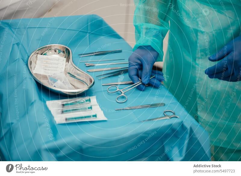 Crop doctor arranging surgical instruments on table before operation man surgeon surgery tool prepare sterile medical operating room professional glove hospital