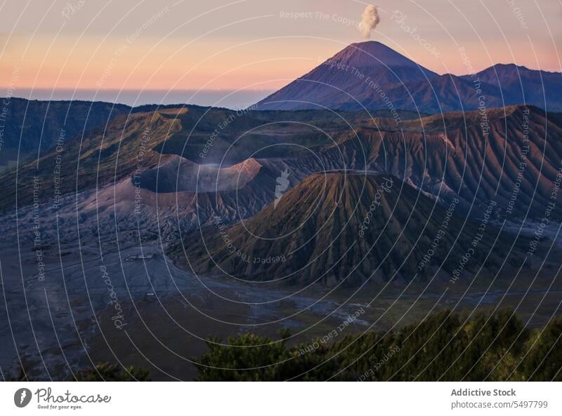 Volcanic mountain with erupting smoke against orange sky in evening time daylight breathtaking volcano highland volcanic landscape nature magma crater vapor