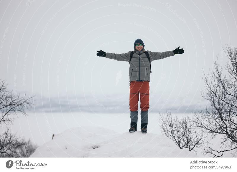 Cheerful man with outstretched arms standing on snowy terrain winter forest nature outerwear happy finland warm clothes cold excited cheerful tree woods