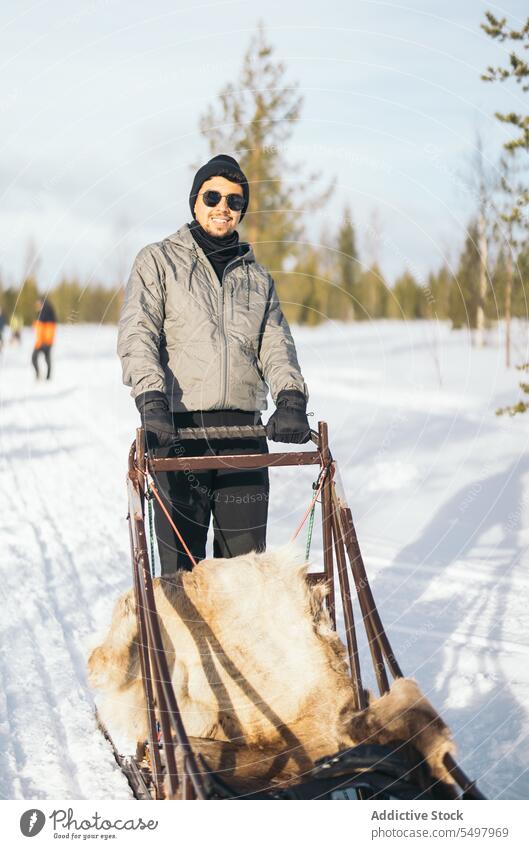 Glad man in sunglasses near sledge traveler winter forest snow road glad portrait male tourist lapland nordic vacation weekend adventure trip explore nature