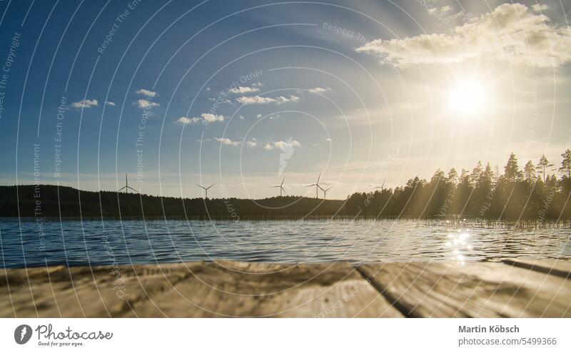 View over a footbridge into the blue water of a lake. Wind turbines in the background. Bathing evening beautiful wind turbines electricity renewable energy dusk