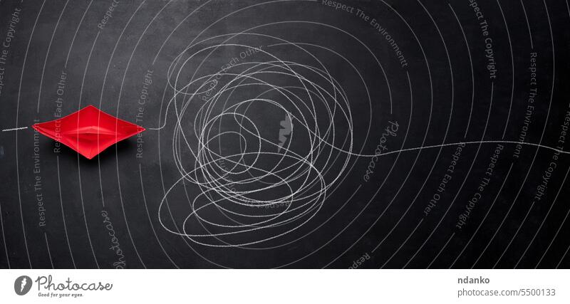 A red paper boat and a tangled trajectory drawn in chalk. The concept of difficult decisions, a long way and overcoming difficulties path solution difficulty