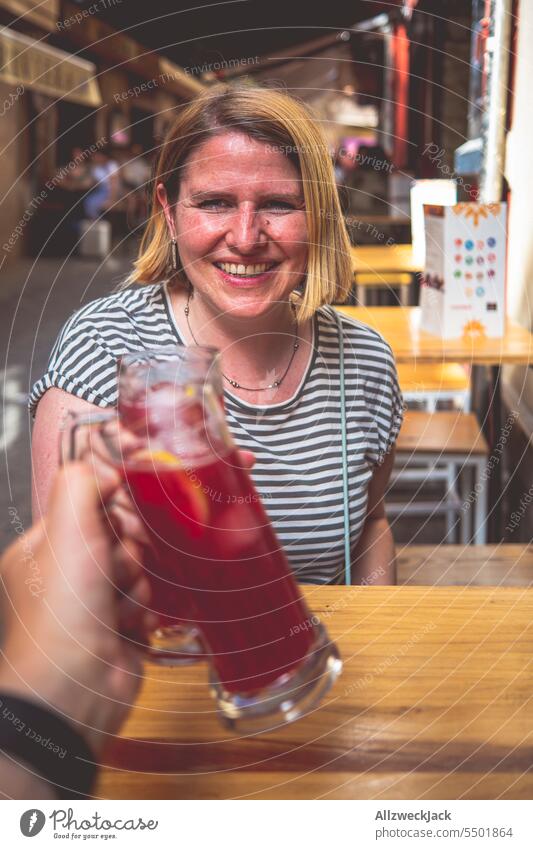 young woman with blonde medium length hair sits at a table and toasts with a glass of Tinto de Verano Granada Red wine Spain Andalucia Bar Tapas bar Refreshment