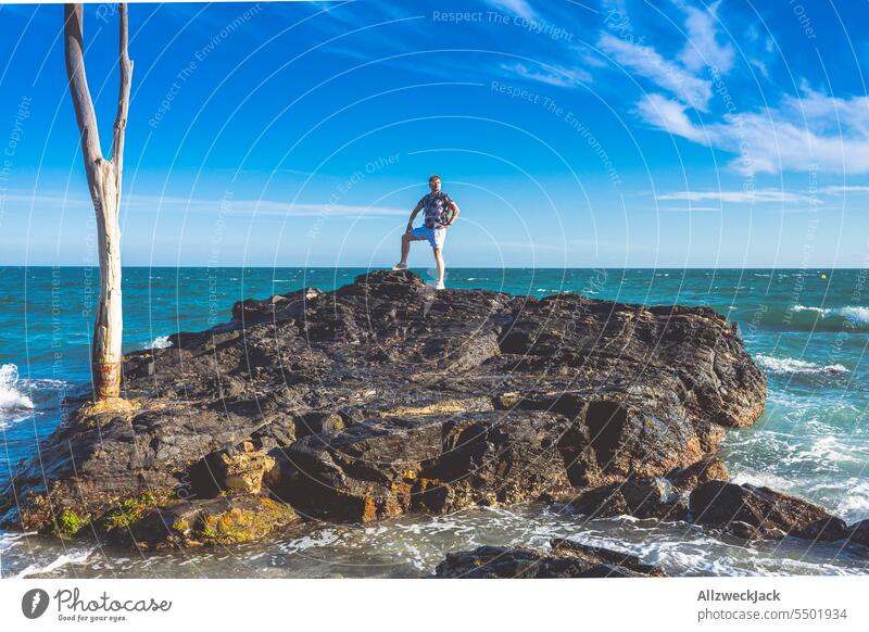 Middle aged man with glasses stands in heroic pose on a rock in the sea Ocean Seashore seaboard rocky Rock Waves Swell coast coastal landscape middle-aged man