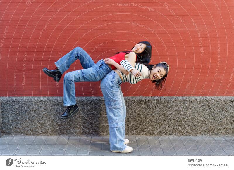 Happy Asian woman lifting friend on back smile cheerful women together fun happy relationship friendship positive female casual ethnic style joy glad stand lady