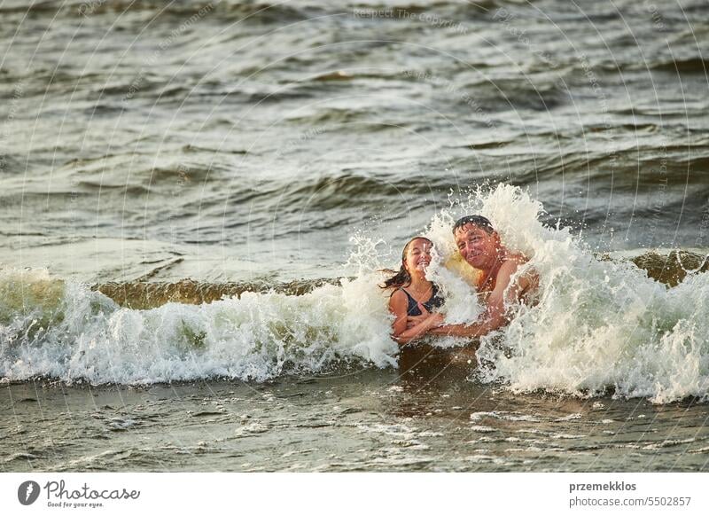 Little girl and her dad playing with waves in the sea. Family summer vacations. Kid playfully splashing with waves. Summer vacation on the beach ocean family