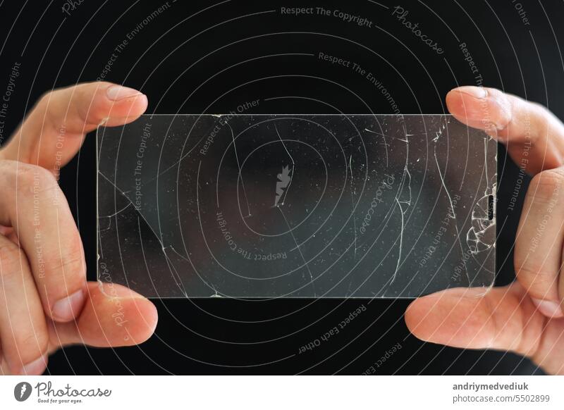 Broken protective glass for smartphone touch screen in hands of phone repairman on black background. Services for gluing and replacement of damaged protective glass. Repair concept