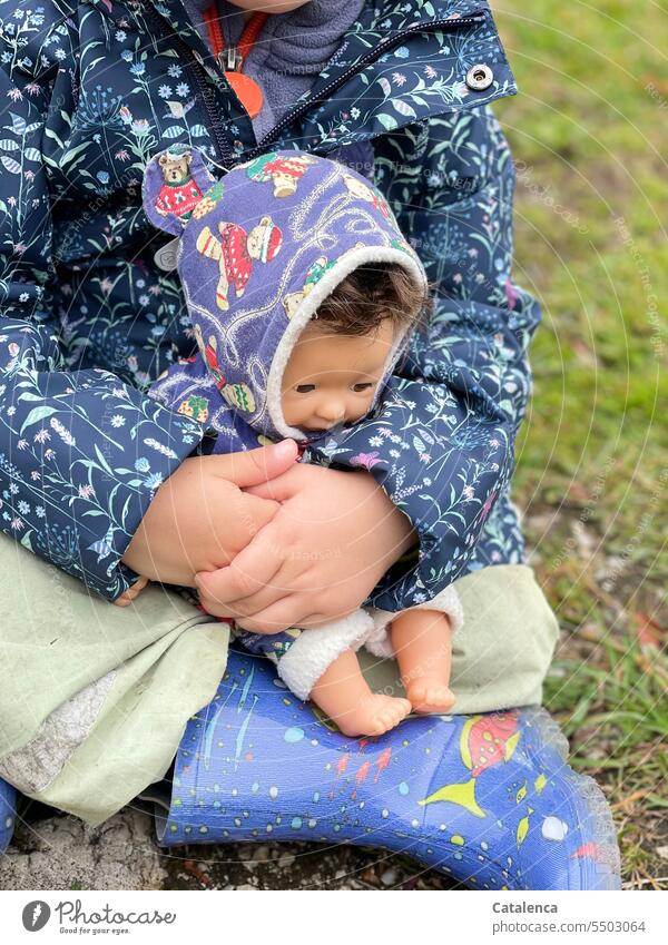 Little girl holding her doll child in her arms Doll Toddler Toys Child Infancy Girl Playing Cute Small Action Sit hands stop Rubber boots Blue Day daylight