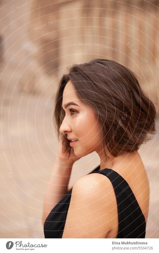 Beautiful brunette woman closeup portrait at street of historic town. Gorgeous girl sightseeing in Europe. Confident woman, solo female traveler. Glamour and chic, fashion and style concept.