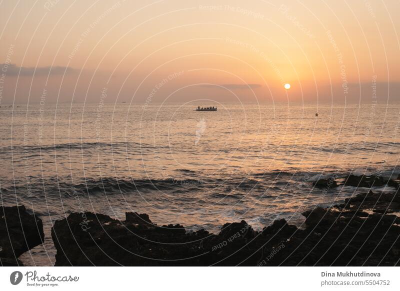 Rowing boat at sunrise over the sea in early morning light. Sun rising over the water on rocky beach. Sunset landscape. Water splashing with waves. ocean nature