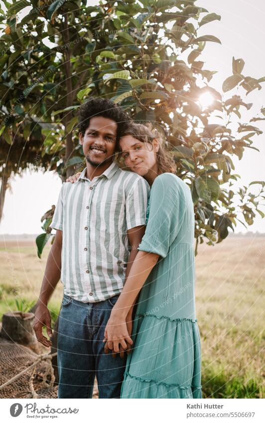 a young woman and a young man holding hands in front of a tree through which the sun rays shine Man Woman romantic Couple Love Together Happy Romance