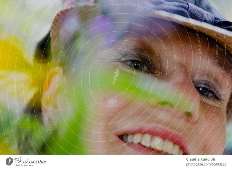 Smiling woman looks at viewer through blurred flowers gardener love of gardens Flower love do gardening artist Gardening Leisure and hobbies plants Woman