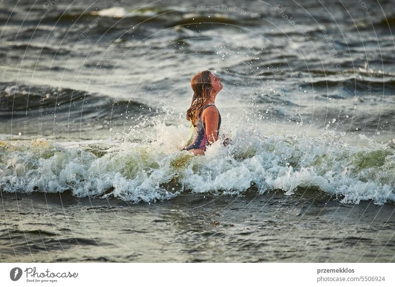 Little girl playing with waves in the sea. Kid playfully splashing with waves. Child jumping in sea waves. Summer vacation on the beach summer vacations ocean