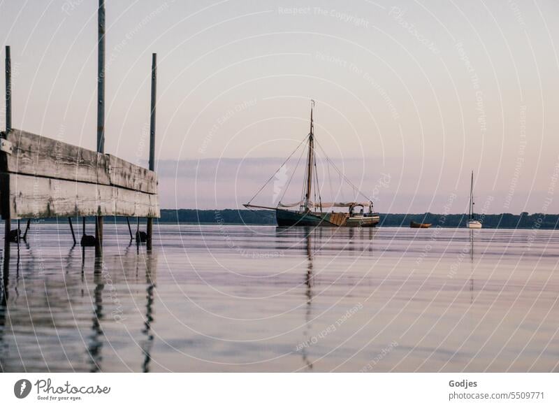 Old sailing ship next to a jetty on the water at dusk, reflection in the water Sailboat Dusk Water Sky Sailing Yacht Ocean vacation Nautical Freedom