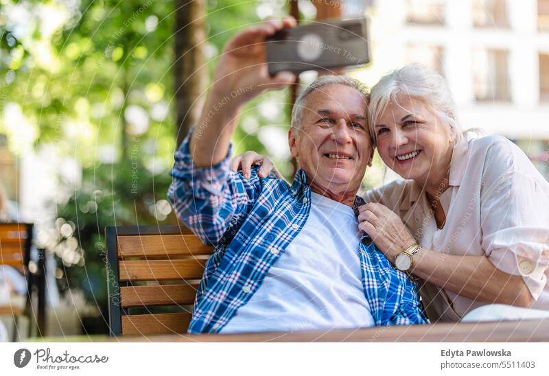 Senior couple sitting at a table in a cafe and using mobile phone people standing healthy city life gray hair enjoy street casual day portrait outside