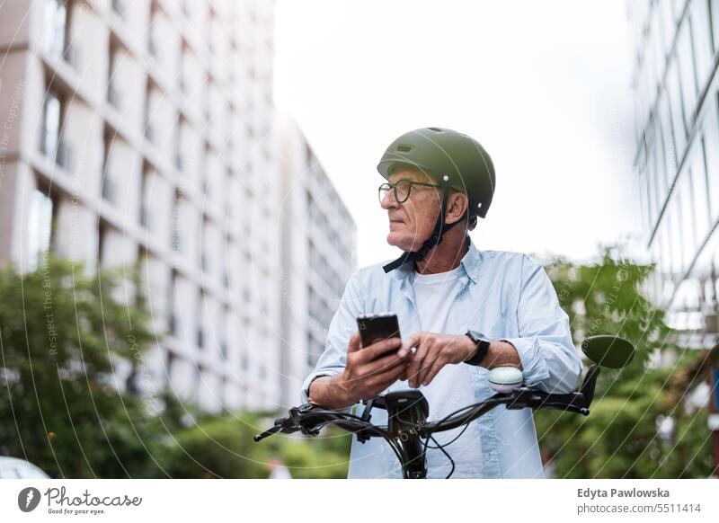 Mature man using mobile phone while riding bicycle in the city people caucasian standing healthy city life gray hair enjoy street casual day portrait outside