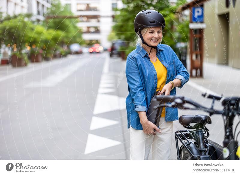 Mature woman changing battery on electric bicycle people caucasian standing healthy city life gray hair enjoy street casual day portrait outside real people