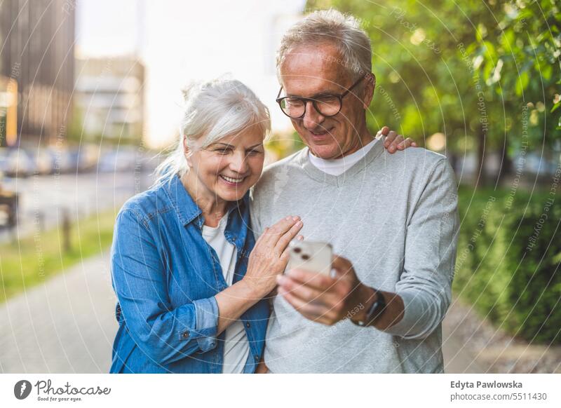 Senior couple using smartphone in the city people caucasian standing healthy city life gray hair enjoy street casual day portrait outside real people