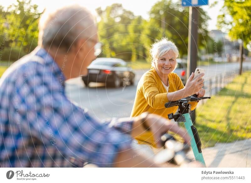 Senior couple riding electric scooters in the city people caucasian standing healthy city life gray hair enjoy street casual day portrait outside real people