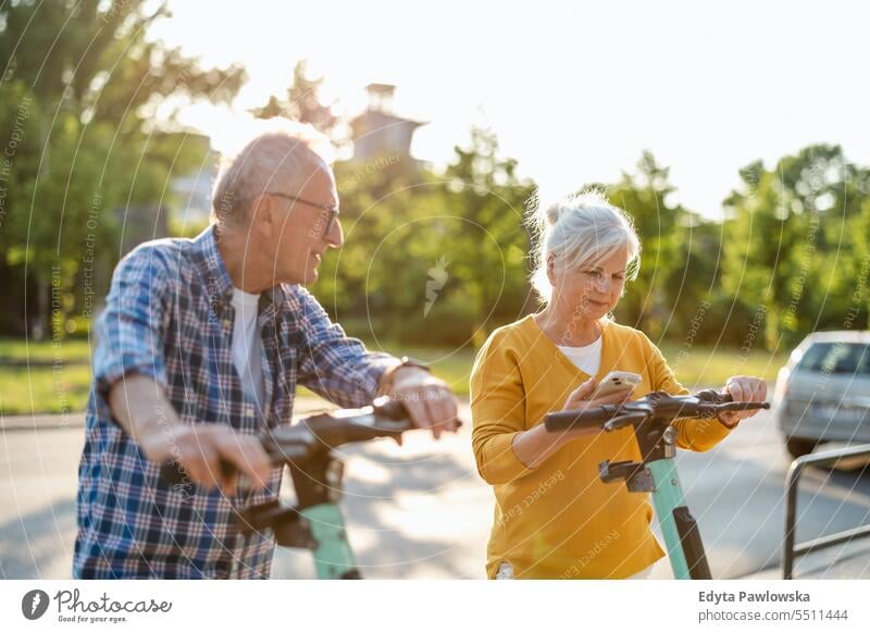 Senior couple riding electric scooters in the city people caucasian standing healthy city life gray hair enjoy street casual day portrait outside real people