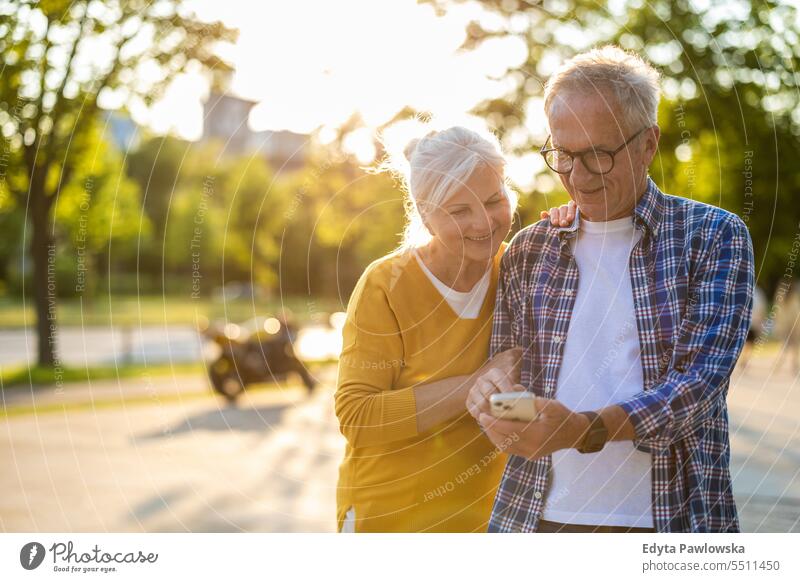 Senior couple using smartphone in the city people caucasian standing healthy city life gray hair enjoy street casual day portrait outside real people